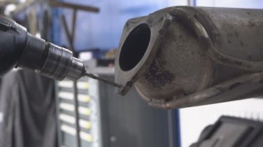 Araba servis istasyonunda metali delme işlemi. Delme aleti, egzoz sisteminin büyük bir metal bölümünde derin bir delik açar. Bir atölyede bir metal ürünü mekanik bir aletle delmek