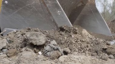 Büyük bir kazıcı kovası taşları dağıtır ve bir inşaat alanındaki toprağı düzleştirir.