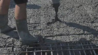 İnşaat alanındaki inşaatçılar yüzeyi beton ve küçük çakıl karışımıyla bir konut inşaatı alanının betonlaşması için döşüyorlar.