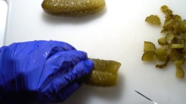 Mutfakta bir aşçı salataya salatalık turşusu keser.