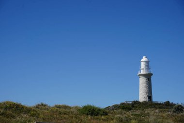 Tepedeki açık mavi gökyüzünün altında beyaz bir deniz feneri manzarası