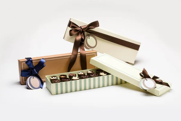 Presentation of handmade chocolate in boxes with different colors and patterns, with ribbons and labels, on a white background