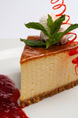 On a white plate, garnished with mint leaves, cheesecake, and strawberry sauce on the side, close-up