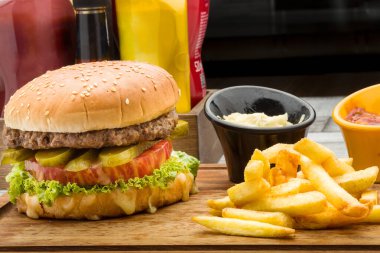 On wooden floor, stripes burger, with french fries, sauces in background