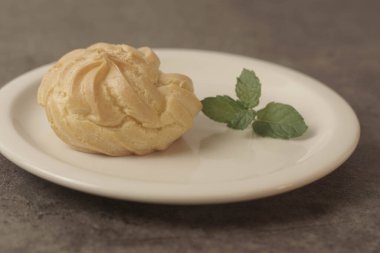 Kue Soes ya da choux la crme beyaz tabakta. Mükemmel şişirilmiş ve kremalı dolgu ile dolu, bu klasik Fransız tatlısının kesinlikle zevkli olacağı kesin. Seçici Odaklanma. Yakın çekim.