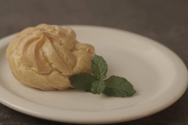 Kue Soes ya da choux la crme beyaz tabakta. Mükemmel şişirilmiş ve kremalı dolgu ile dolu, bu klasik Fransız tatlısının kesinlikle zevkli olacağı kesin. Seçici Odaklanma. Yakın çekim.