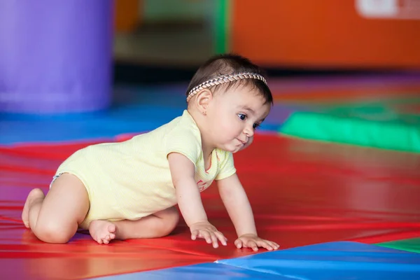 stock image Beautiful ten months baby girl crawling on a colorful background. Early stimulation for toddlers concept.