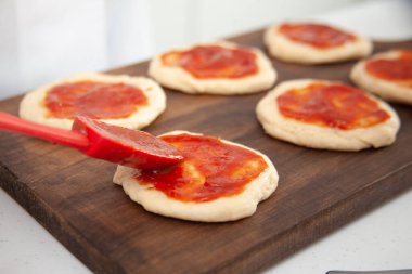 Kıdemli kadın gerilmiş hamura pizza sosu ekliyor. Lezzetli ev yapımı mini pizzalar..