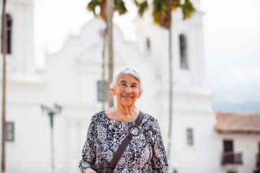 Senior adult woman at the central square in the city of Guaduas located in the Department of Cundinamarca in Colombia. Senior lifestyle. Senior travel concept. clipart