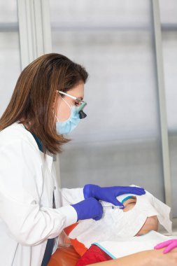 Deri lezyonu çıkarma prosedürü. Dermatolog, genç bir erkek hastanın yüzünde iyi huylu deri lezyonunu temizliyor. Lokal anestezi.