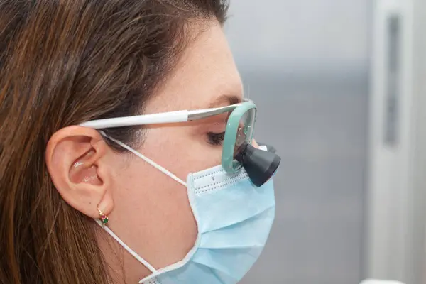 stock image Close up of a female dermatologist face while suturing a patient during a small surgery wearing a binocular loupe.