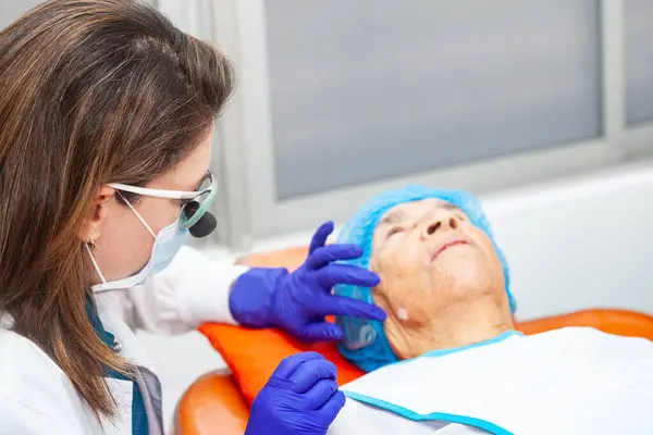 stock image Dermatologist carrying out a skin biopsy on the face of a senior adult patient