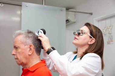 Dermatologist performing a trichoscopy to a senior male patient. clipart