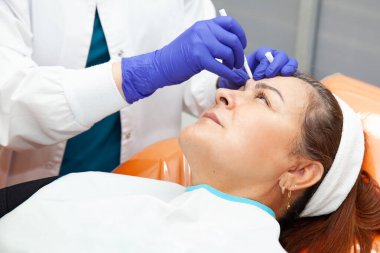 Dermatolog, orta yaşlı bir kadın hastaya botulinum toksini uygulanması için enjeksiyon noktalarını işaretliyor. Estetik tıp