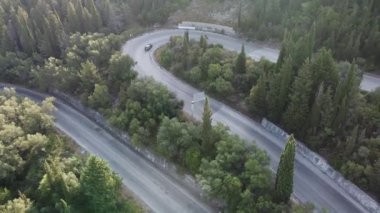 AERIAL: cars, buses and motorcycles driving on zig zag winding road through green lush forest vegetation on the Island of Corfu, Greece