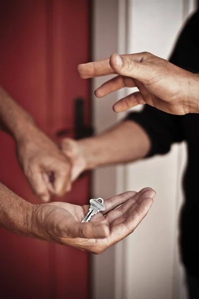 close up of hands accepting a house key to new home holding hands in background