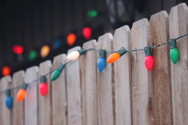 Ahşap bir çitin kenarına asılmış renkli Noel ışıkları
