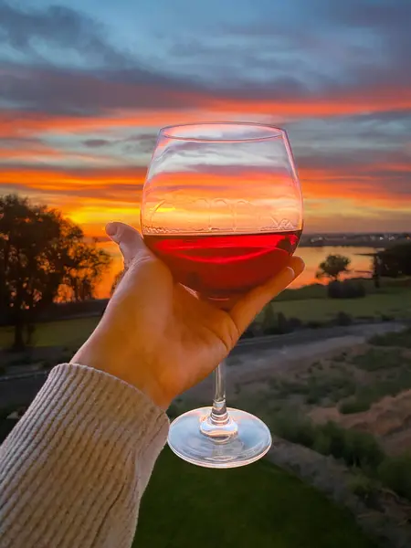 Şarap kadehi kırmızı şarapla birlikte canlı bir günbatımına karşı tutuluyor.