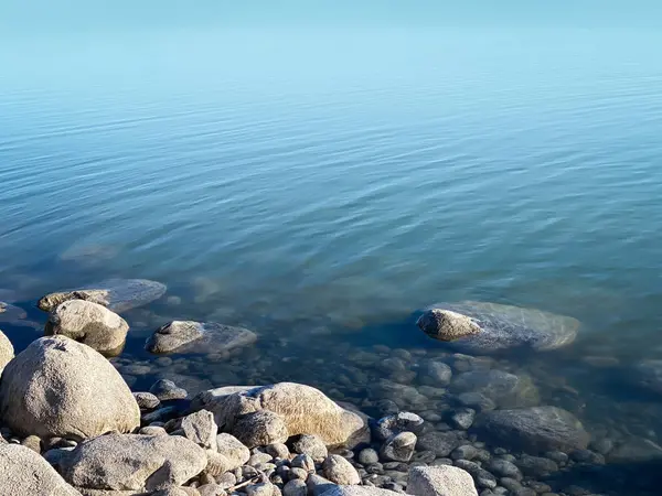 Gölün kıyısındaki kayalıklarda durgun mavi su ve birkaç hafif dalgalanma.