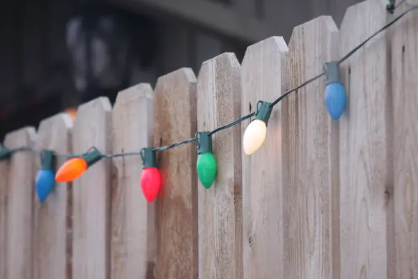 Ahşap bir çitin kenarına asılmış renkli Noel ışıkları