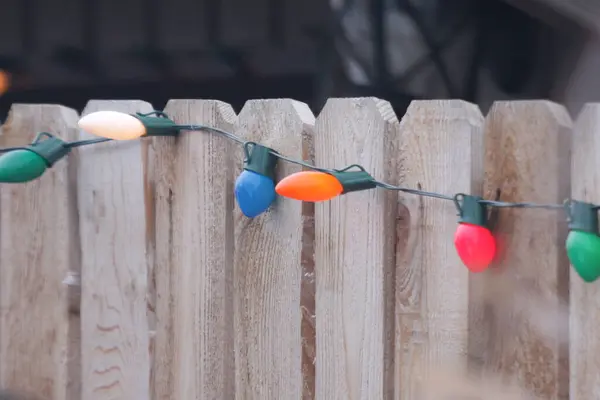 Ahşap bir çitin kenarına asılmış renkli Noel ışıkları