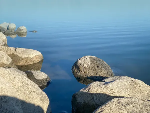 Gölün kıyısındaki kayalıklarda durgun mavi su ve birkaç hafif dalgalanma.