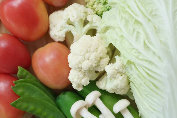 En üstteki düz tabakta taze sebze karışımı Çin lahanası, mantar, domates, havuç, yeşil bezelye, salatalık, brokoli ve ahşap yuvarlak yeşil arka plan. Vegan ev yapımı sağlıklı vitamin organik gıda..