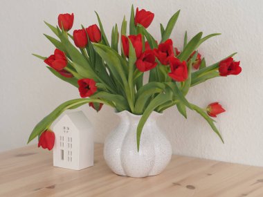 Vazoda kırmızı laleler ve yanında beyaz hatıra evi. 