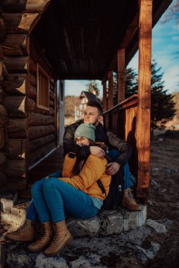 Bir kadın ve bir erkek kır evinin önünde yürüyüş yaparken dinleniyorlar.