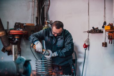 Özel kıyafet ve gözlüklü bir çilingir üretim işinde çalışıyor. Açı öğütücüyle metal işleme. Metal işçiliğinde kıvılcımlar