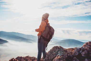 a hiking girl with a backpack on her back watches the morning from the top of the mountain