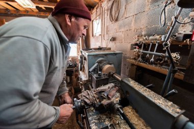 A senior man procesing wood on a lathe and making wooden dishes in the workshop. 