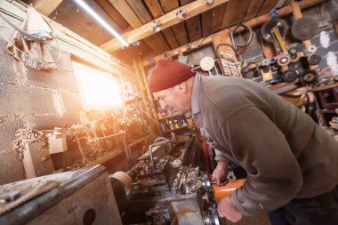 A senior man procesing wood on a lathe and making wooden dishes in the workshop. 