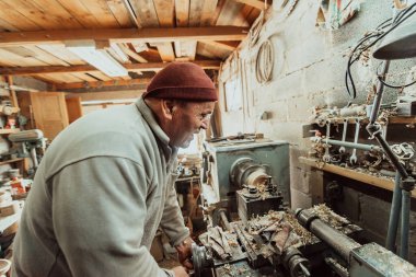 A senior man procesing wood on a lathe and making wooden dishes in the workshop. 