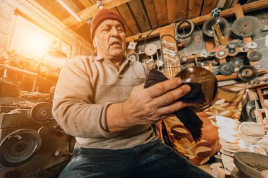 A senior man sitstingin the workshop and smearsing wooden utensils with linseed oil. 