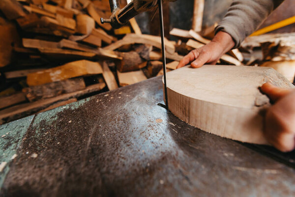 A senior man processing wood on a machine in an outdoor workshop. 