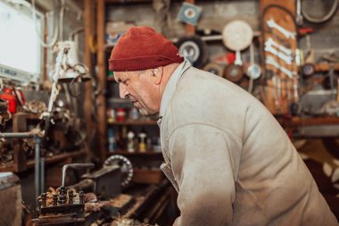 A senior man procesing wood on a lathe and making wooden dishes in the workshop. 