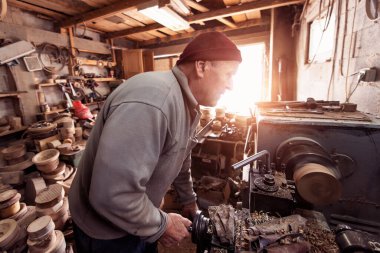 A senior man procesing wood on a lathe and making wooden dishes in the workshop. 