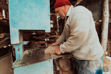 A senior man processing wood on a machine in an outdoor workshop. 
