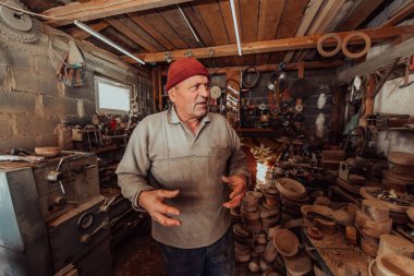 A senior man processing wooden dishes in the workshop in the traditional manual way. 