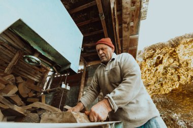 A senior man processing wood on a machine in an outdoor workshop.