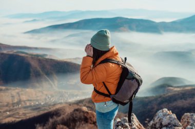 a hiking girl with a backpack on her back watches the morning from the top of the mountain
