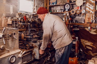 A senior man procesing wood on a lathe and making wooden dishes in the workshop.