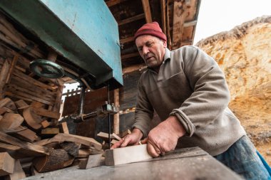 A senior man processing wood on a machine in an outdoor workshop. 