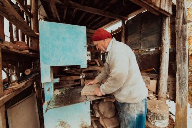 A senior man processing wood on a machine in an outdoor workshop. 