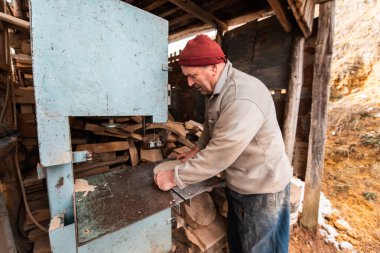 A senior man processing wood on a machine in an outdoor workshop. 