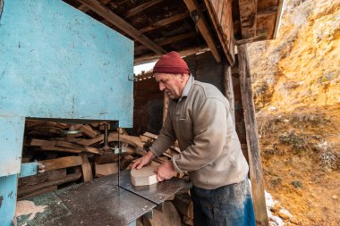 A senior man processing wood on a machine in an outdoor workshop. 