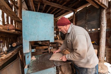 A senior man processing wood on a machine in an outdoor workshop. 