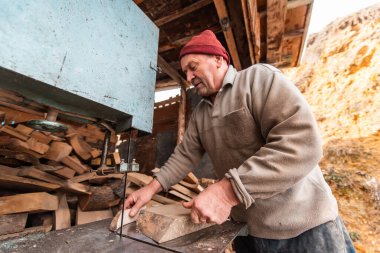 A senior man processing wood on a machine in an outdoor workshop. 