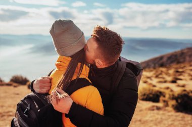 a young couple embracing standing on top of a mountain